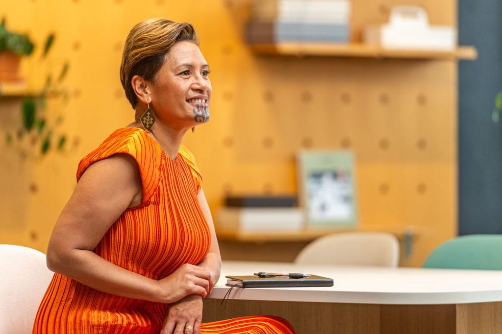Image of Rachel Petero sitting at a desk wearing an orange dress.